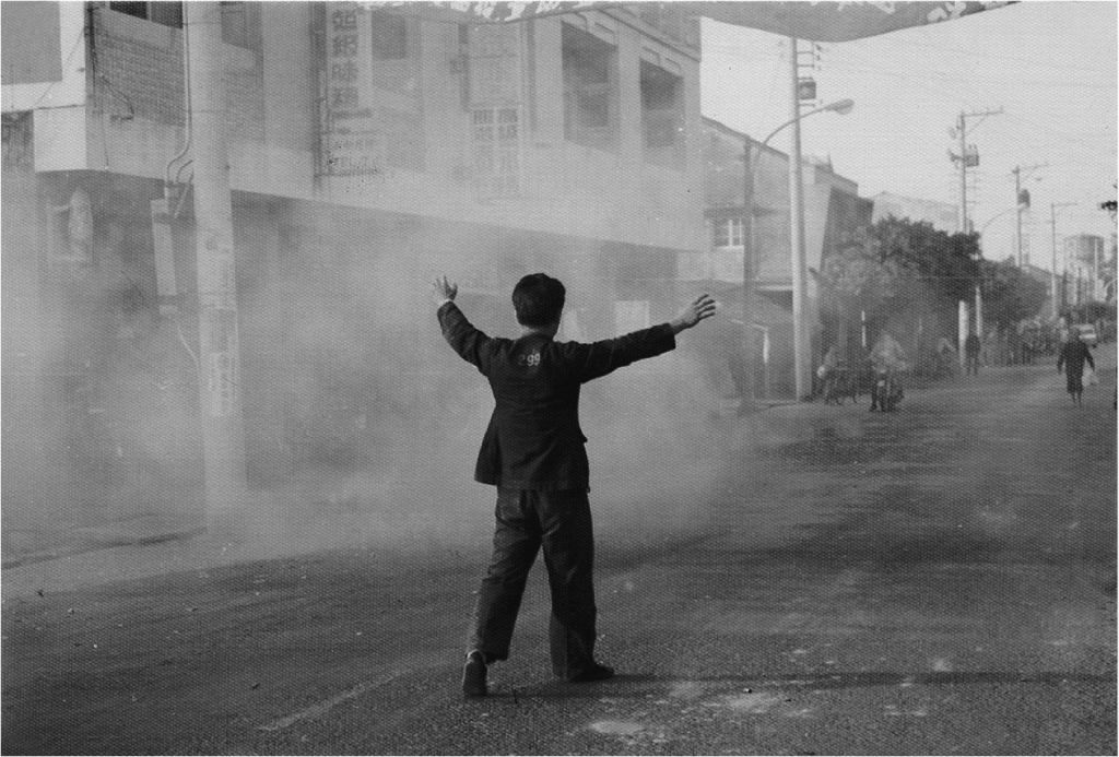 1977.11.19蘇東啟著囚服在雲林縣北港鎮街道拜票，在鞭炮煙硝中伸雙手抗議。（771119N29／施明德提供）