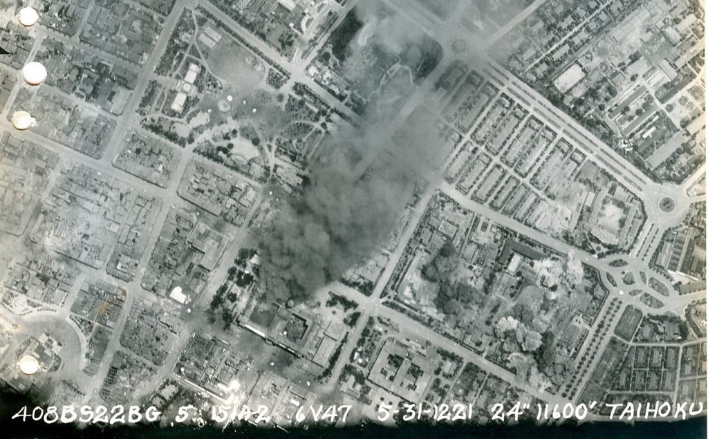 「台北大空襲」的航空圖局部。圖中冒黑煙的建築物為總督府，其下方右側的「ㄈ」字型建築物即為遞信部。（Photo Credit: Wikimedia Commons）
